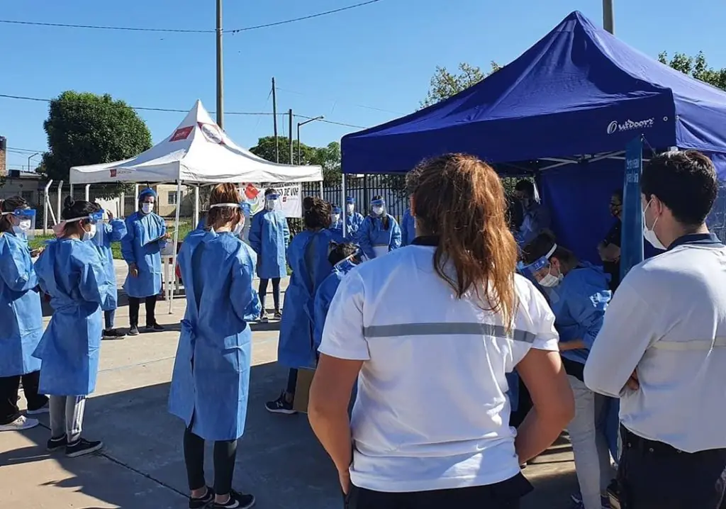 Personas con batas médicas participan en una actividad de salud comunitaria bajo una carpa al aire libre.