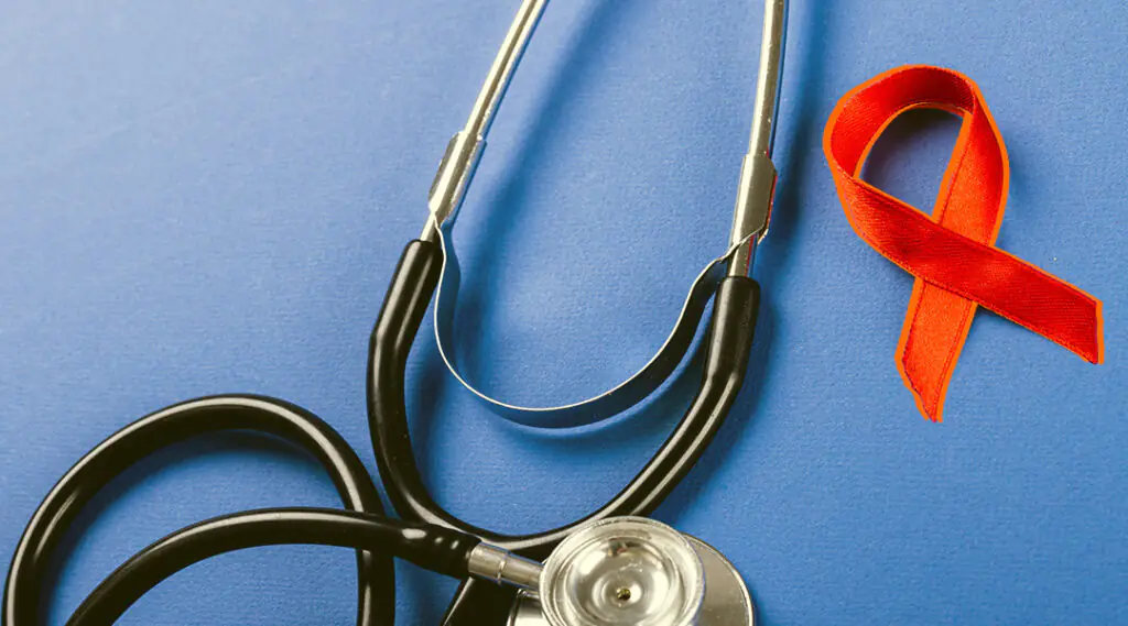 Estetoscopio sobre fondo azul junto a lazo rojo de concientización sobre el VIH.