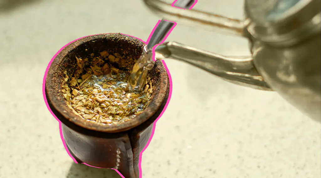 Agua caliente se vierte sobre un mate con yerba, ilustrando una escena cotidiana.