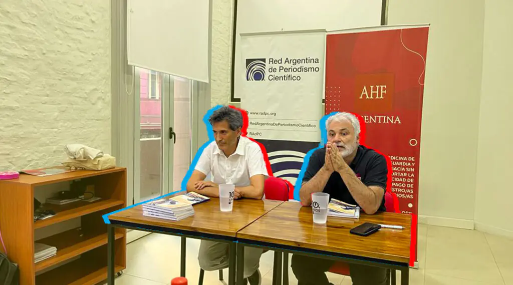 Dos personas participan en una charla informativa frente a una mesa con material educativo de AHF.