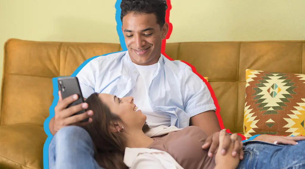 Pareja relajada en el sofá mientras el hombre usa su teléfono móvil.