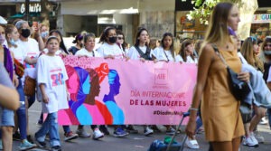 Personas marchan con una bandera que dice “8M Día Internacional de las Mujeres” durante una movilización.