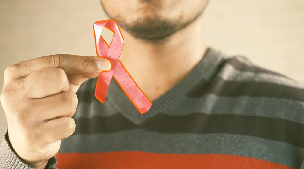 Persona sostiene un lazo rojo de concientización sobre el VIH frente a su pecho.