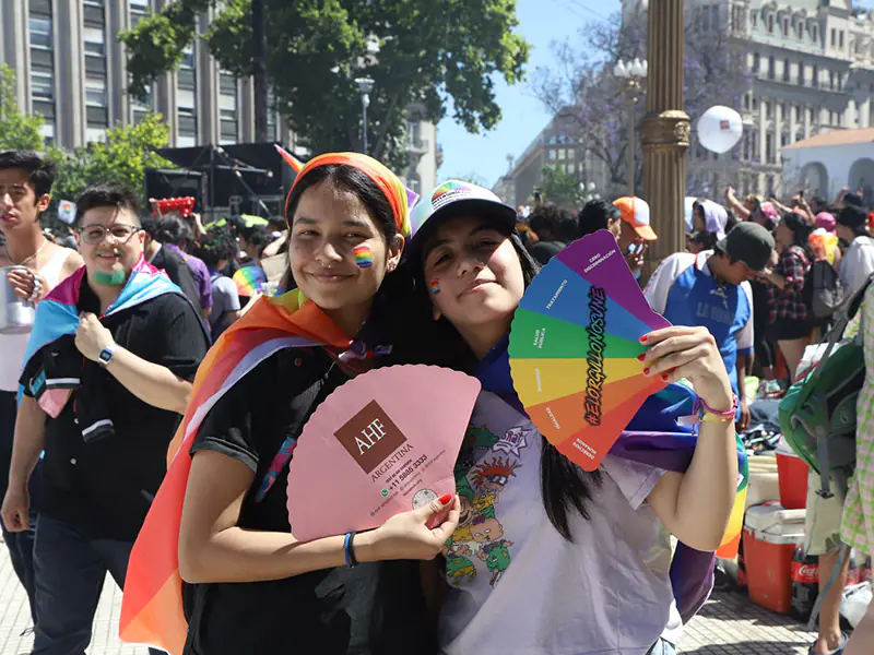 Participantes con banderas del orgullo sostienen abanicos de AHF Argentina durante marcha por la diversidad.
