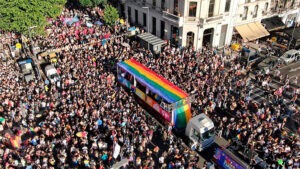 Multitud rodea un vehículo con los colores de la bandera LGBTQ+ durante una marcha del orgullo.