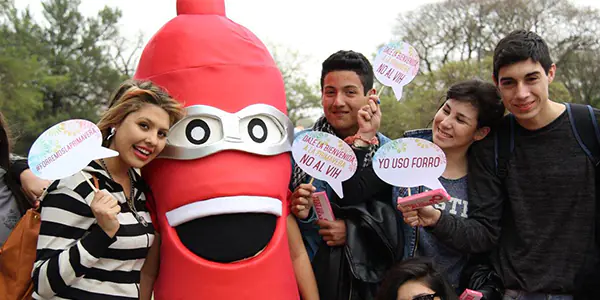Participantes sostienen mensajes de prevención junto a preservativo inflable en campaña juvenil de AHF Argentina.