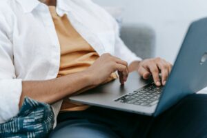 Person in a white shirt typing on a laptop resting on their lap on a couch/sofa outlet”,
